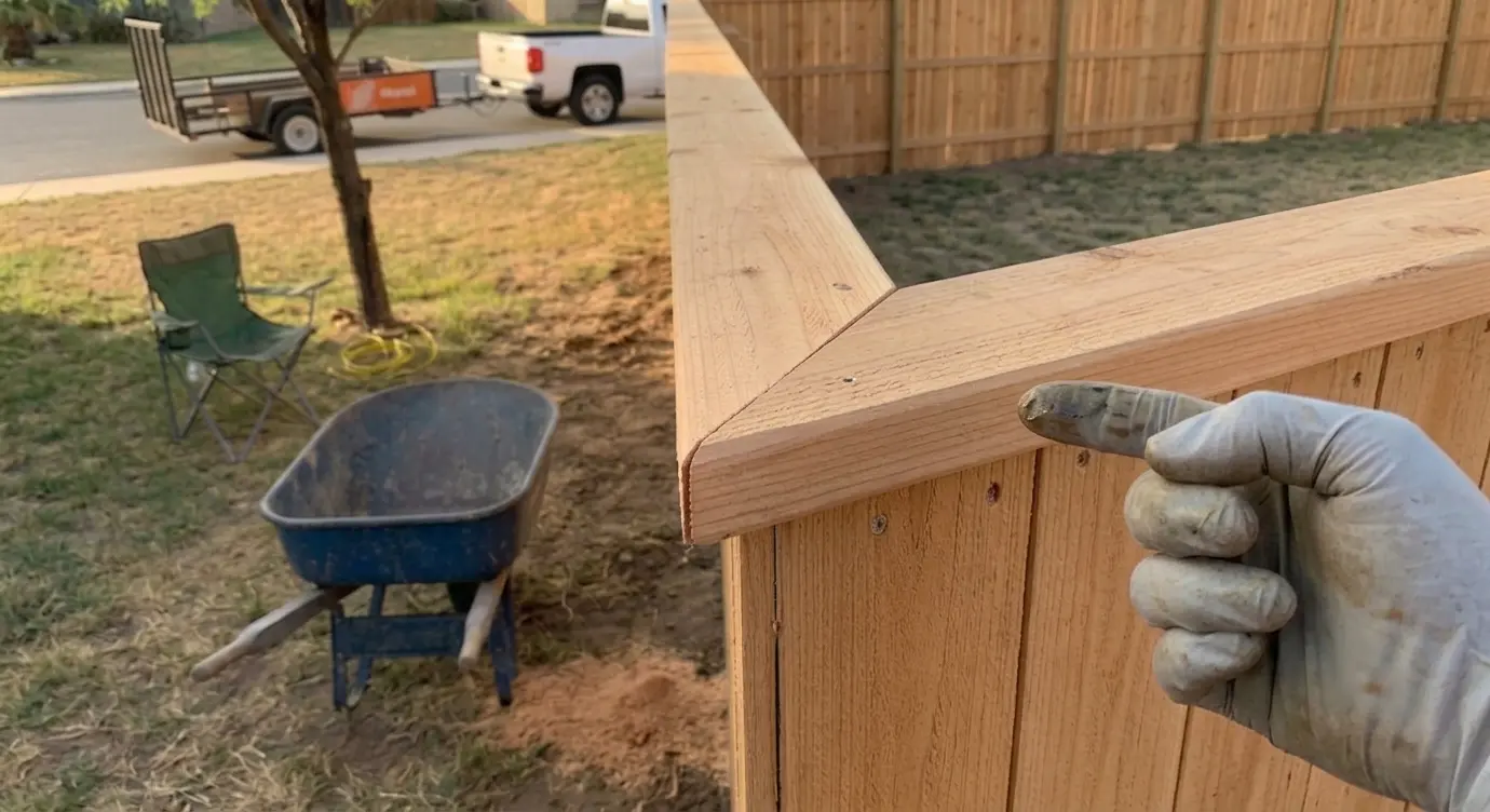 Cedar cap detail at a wood privacy fence corner in Laredo; gloved hand visible at frame edge.
